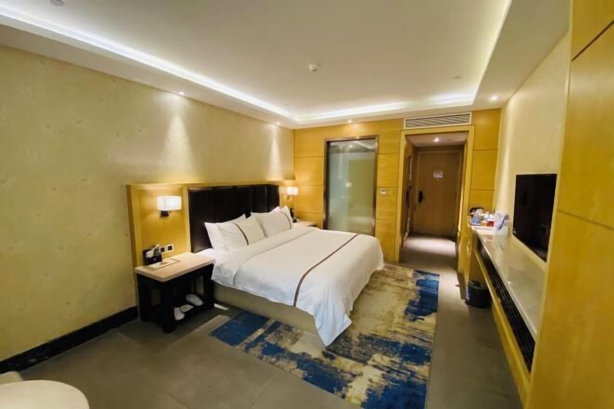 Habitación de hotel con cama, mesita de noche, lámpara, televisor y baño.