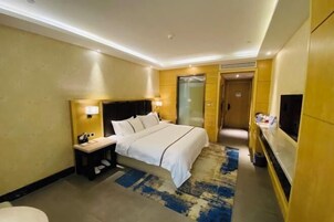 Habitación de hotel con cama, mesita de noche, lámpara, televisor y baño.