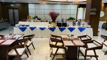 Un salón de banquetes con mesas dispuestas para una comida, una zona de bufé con comida y bebidas, y una decoración central.
