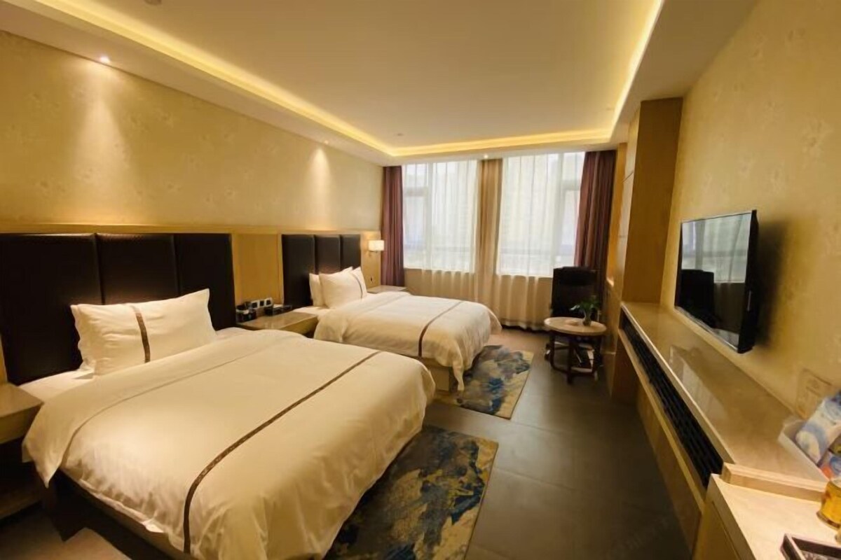 Habitación de hotel con dos camas, televisión, escritorio y ventana con cortinas.