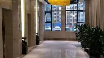 Un hall d’hôtel avec un sol en marbre, de grandes fenêtres et un lustre jaune.