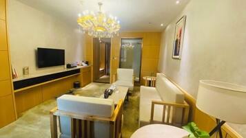 A modern hotel room with a flat-screen TV, a chandelier, a sofa, a dining table, and a lamp.