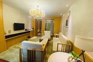 Una habitación de hotel moderna con una televisión de pantalla plana, una araña, un sofá, una mesa de comedor y una lámpara.