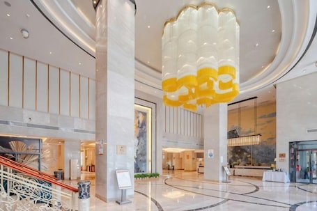 A spacious lobby with a central staircase, large columns, and a distinctive yellow and white chandelier.. Fuli Hotel