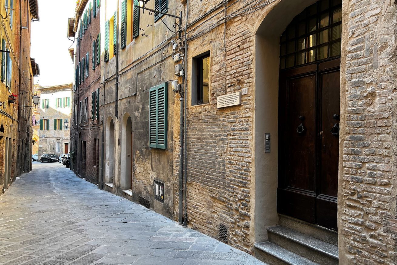 Una calle estrecha con edificios de piedra, una puerta de madera y un cartel en la pared.