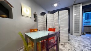 A dining area with a glass table and colorful chairs, a decorative wall, and a view of the outside. - The little house on franciosa street (Siena)