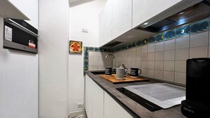 A compact kitchen with white cabinets, a black range hood, a coffee maker, and a decorative backsplash. - The little house on franciosa street (Siena)