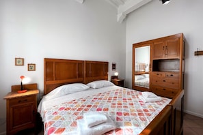 A bedroom with a wooden bed, a nightstand with a lamp, a dresser, and a mirror. - Sperandie—within the city walls (Siena)