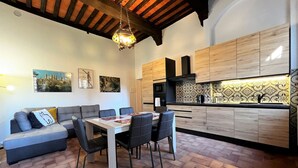 A modern kitchen with wooden cabinets, a dining area with a table and chairs, and a cozy seating area with a sofa. - Sperandie-inside the walls (Siena)