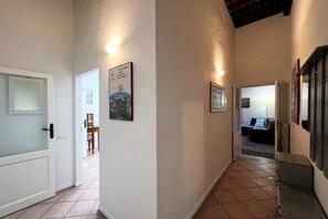 A hallway with white walls, tiled flooring, and a door on the left. There are framed pictures on the walls and a small table with chairs in the background. - Sperandie—within the city walls (Siena)