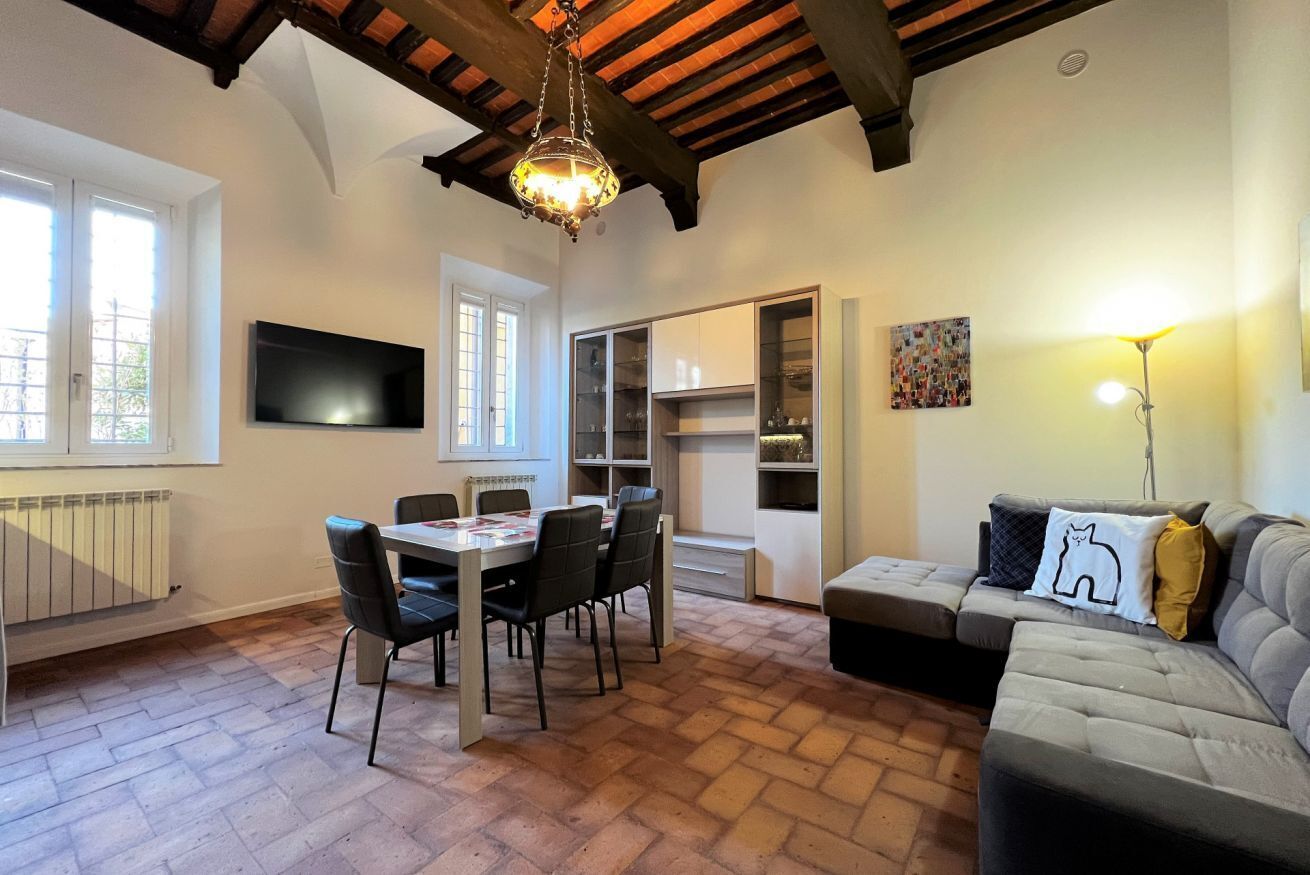 Zona pranzo con tavolo e sedie, un divano, una TV a muro e un lampadario.