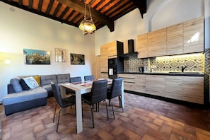 A modern kitchen with wooden cabinets, a dining area with a table and chairs, and a cozy seating area with a sofa. - Sperandie—within the city walls (Siena)