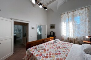 A bedroom with a bed, a bedside table, a mirror, and a door leading to a bathroom. - Sperandie—within the city walls (Siena)
