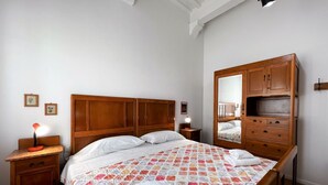 A bedroom with a wooden bed, a nightstand with a lamp, a dresser, and a mirror. - Sperandie-inside the walls (Siena)