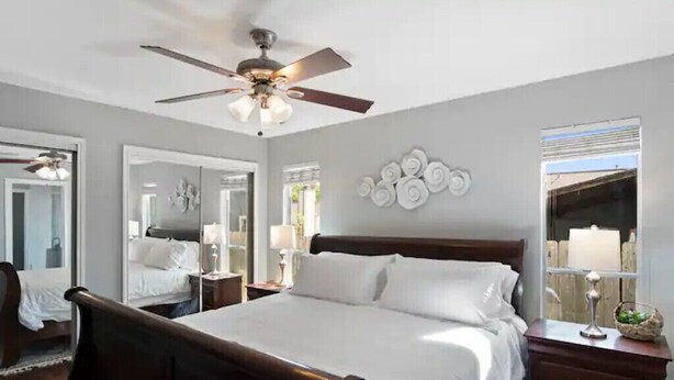 Ein ordentlich eingerichtetes Schlafzimmer mit einem großen Bett, einem Deckenventilator, einem Spiegel und einer Wanddekoration.