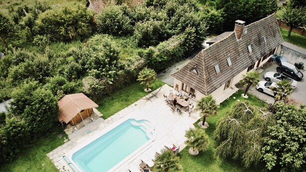 Luchtbeeld van een woonhuis met een zwembad, tuinmeubilair en een overdekt terras.