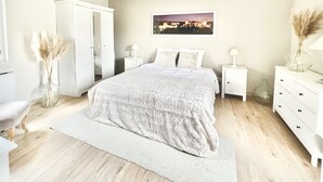 Een slaapkamer met een groot bed, een witte garderobe, nachtkastjes met lampen en een stadsgezichtschilderij aan de muur.