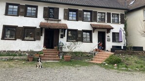 A two-story house with a tiled roof, multiple windows with shutters, and a front entrance with steps leading to a door. - Family-friendly apartment in an old farmhouse (Steißlingen)