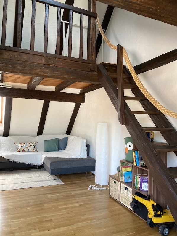 Ein Loft-Zimmer mit einer Holztreppe, einer Couch, einem Bücherregal und einem Spielzeugbagger.