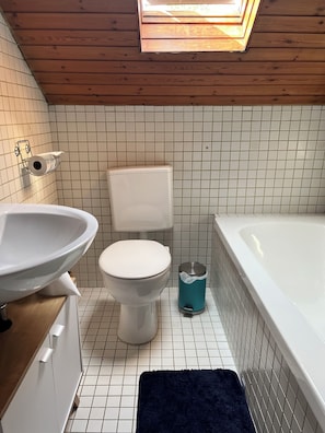 Et badeværelse med toilet, vask og badekar.