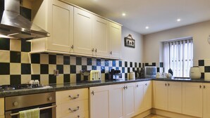 A kitchen with white cabinets, a checkered backsplash, a stove, and a window with blinds.