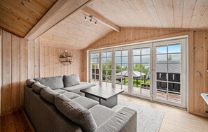 A cozy room with a sectional sofa, a small table, and large windows offering a view of a deck and mountains. - 4 bedroom cozy home in Meisingset (Meisingset)