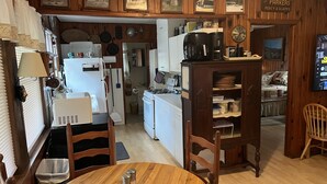 A cozy kitchen with wooden cabinets, a dining area with a wooden table and chairs, and a living area with a bed and a TV. - Cabin with private lake access on Cedar Cliff Lake (Tuckasegee)