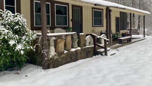 A snow-covered wooden cabin with a porch, stone wall, and a bench. - Cabin with private lake access on Cedar Cliff Lake (Tuckasegee)