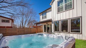 A backyard with a hot tub, wooden fence, and a house with large windows.