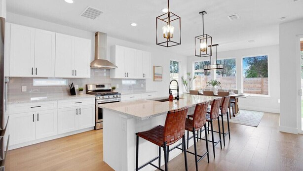 A modern kitchen with white cabinets, a large island with bar stools, stainless steel appliances, and pendant lighting.
