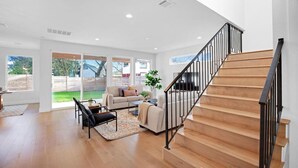 A spacious living room with a wooden staircase, a sofa set, and a large sliding glass door leading to a backyard.