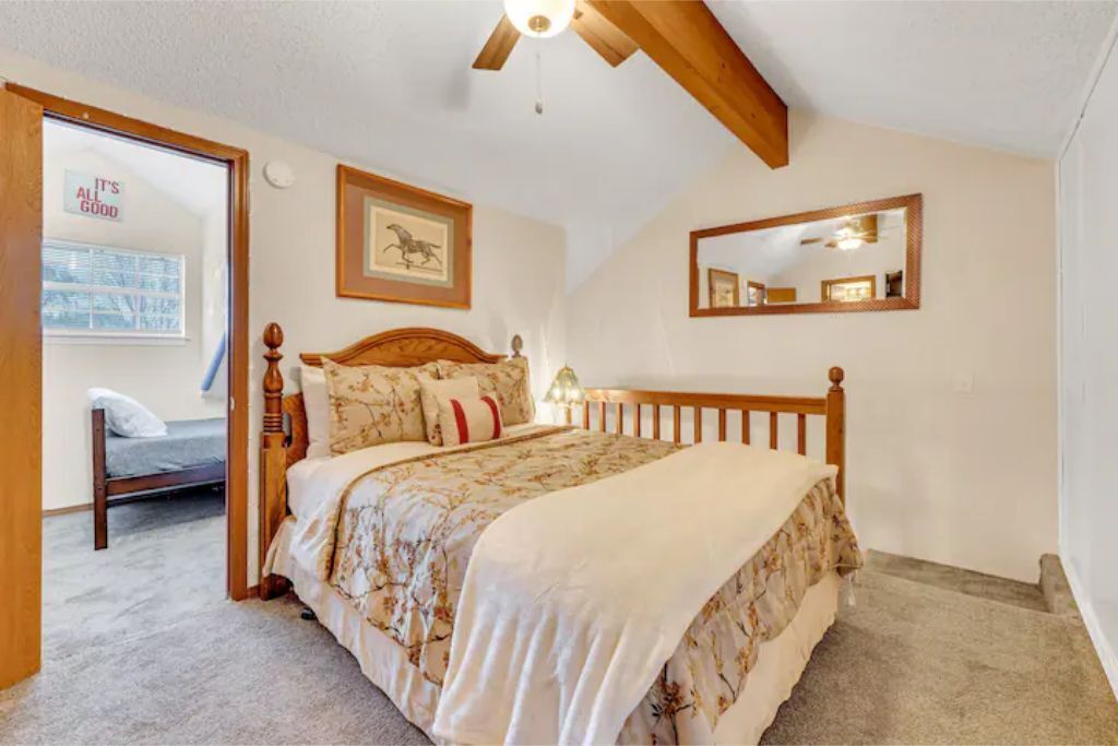 Una camera da letto con un letto di legno, una ventola a soffitto, un quadro incorniciato e uno specchio appeso al muro.