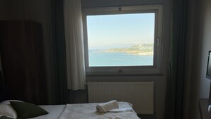 A hotel room with a large bed, a view of the sea, a radiator, and a television. - Ganita Life Hotel (Trabzon)