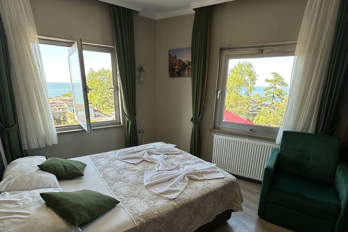 Une chambre à coucher comprenant un lit, une chaise et deux fenêtres donnant sur la mer.
