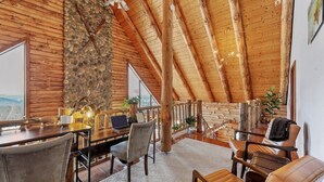 A spacious room with a high wooden ceiling, a stone wall, and a large window offering a view. - Berkshire Mountain Top Chalet (North Adams)