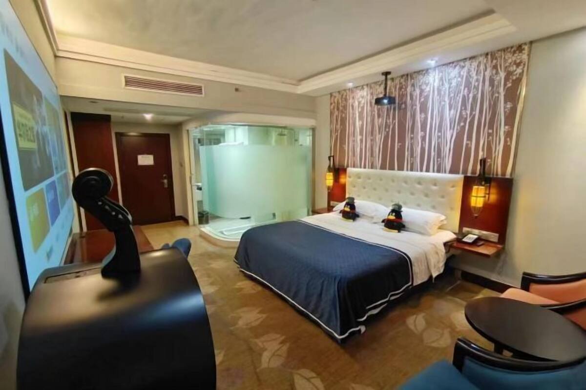 Habitación de hotel con cama, escritorio, silla, zona de ducha y pared con estampado floral.