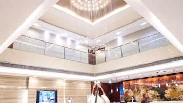 A hotel lobby with a high ceiling, a chandelier, a reception desk, and a large screen.