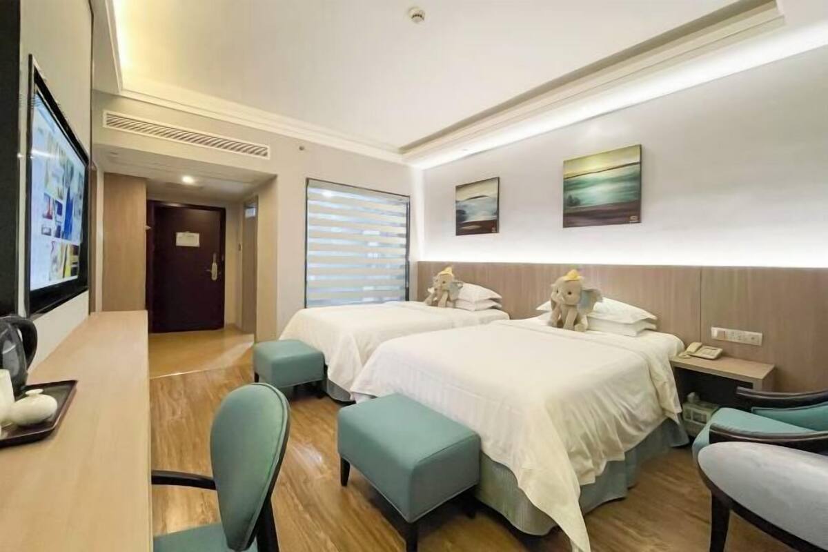 Habitación de hotel con dos camas, un escritorio y una silla. Hay dos cuadros en la pared y una ventana con persianas.