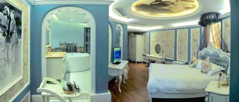 A hotel room with a large bed, a desk with a computer, a chair, and a television.