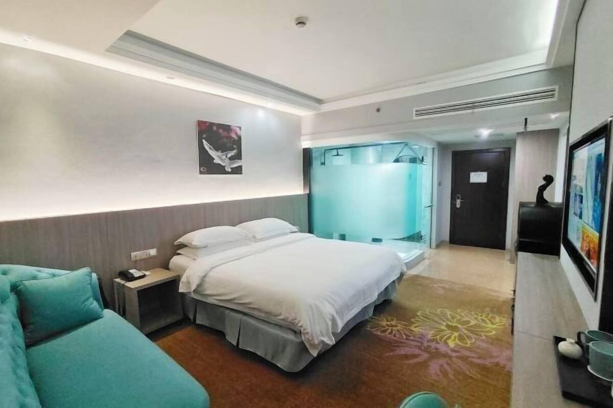 Una habitación de hotel moderna con una cama, una mesita de noche pequeña, una silla y un área de ducha.