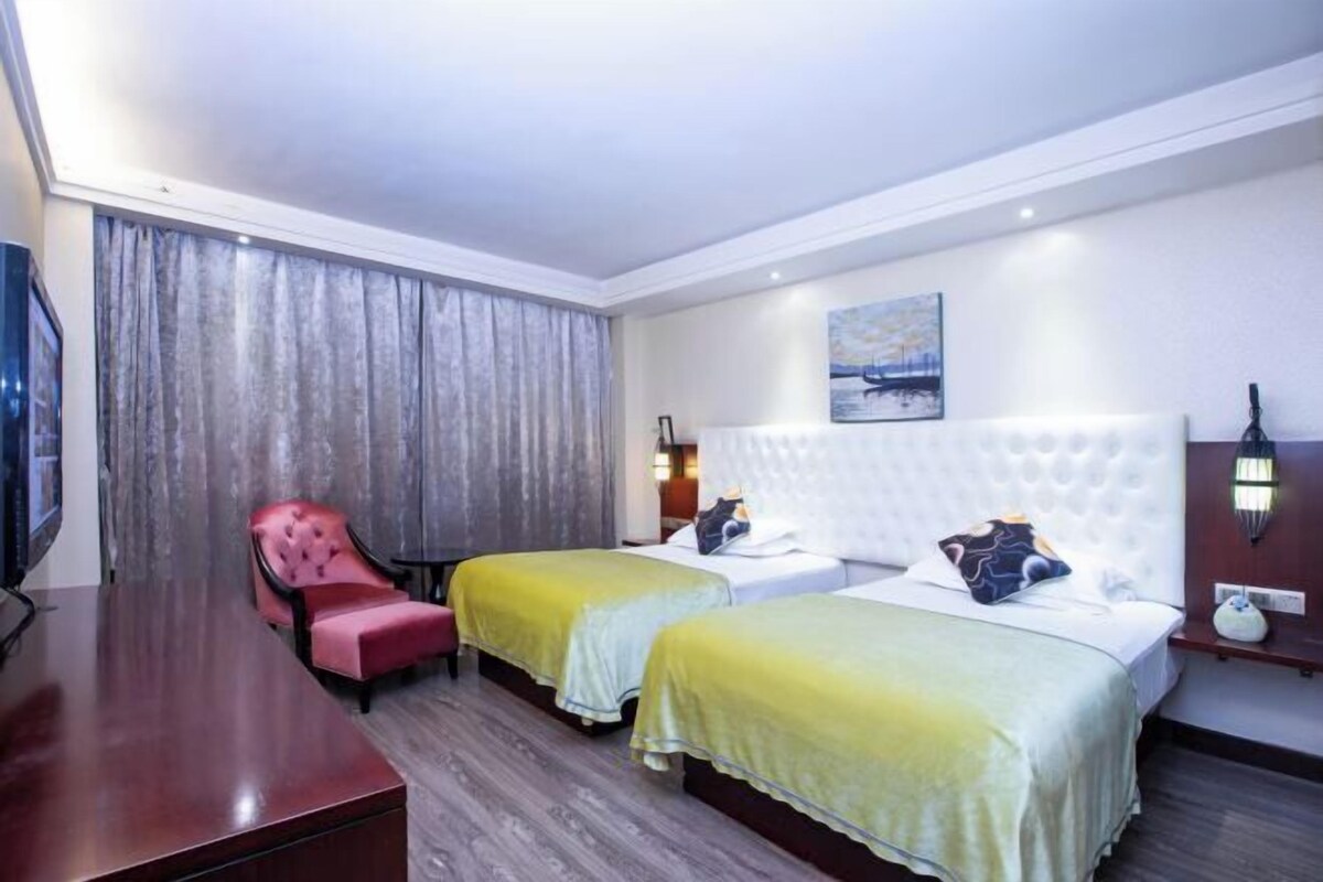 Habitación de hotel con dos camas, un sillón rojo, un escritorio de madera y un cuadro en la pared.