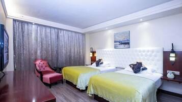 Habitación de hotel con dos camas, un sillón rojo, un escritorio de madera y un cuadro en la pared.