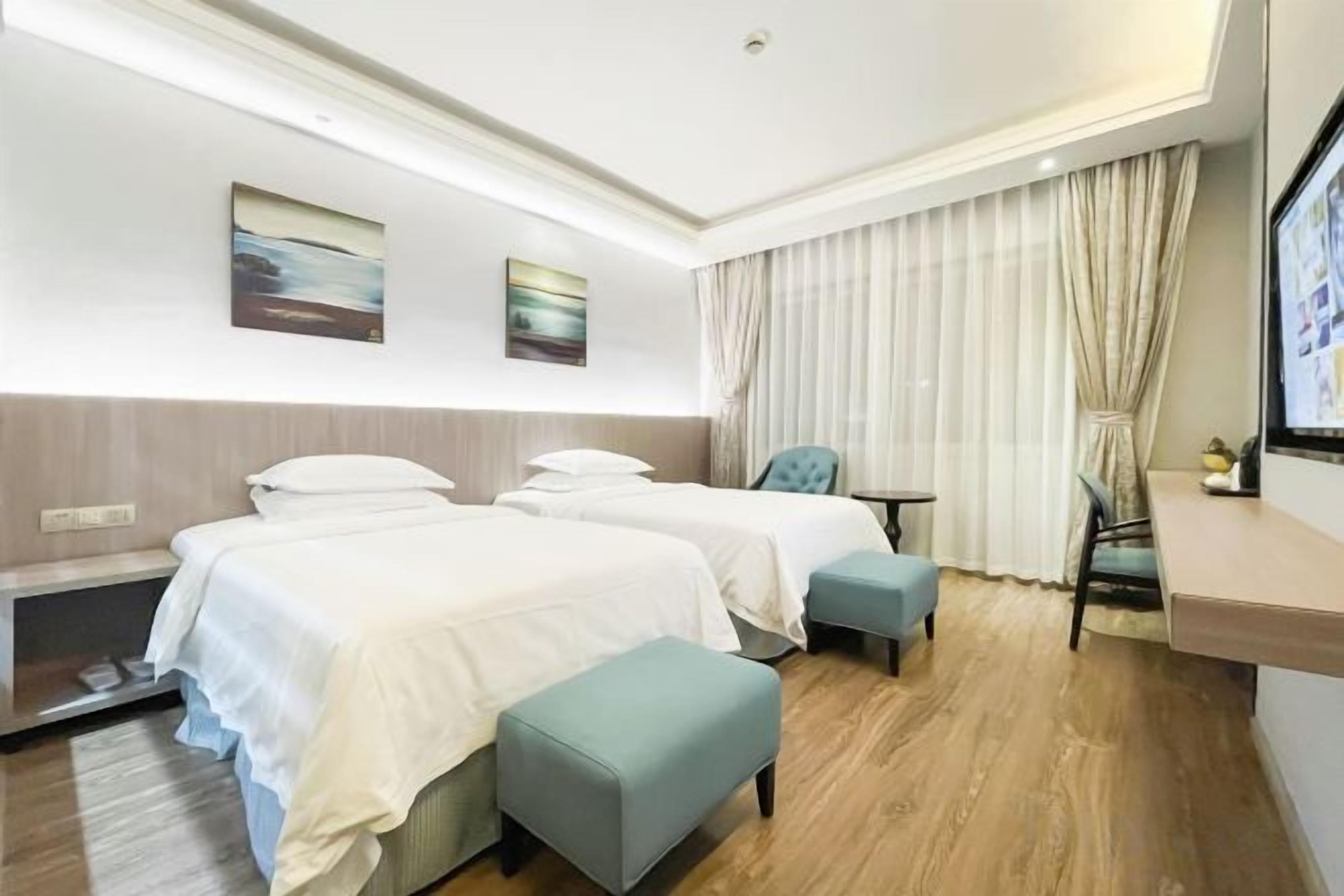 A hotel room with two beds, a desk, a chair, and a TV.