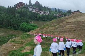 A group of people in traditional attire on a terraced hillside with a building in the background. - Longji Rice Terraces Weila Homestay (Longsheng)