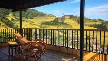 A wooden deck with a wicker chair and a small table, overlooking terraced fields.