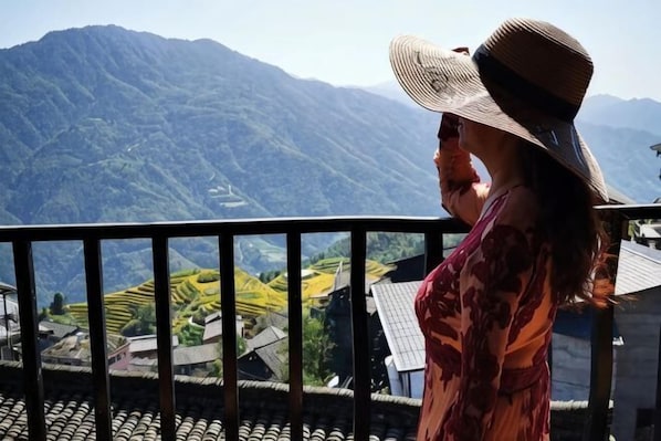 A person on a balcony overlooking a mountainous landscape with terraced fields.
