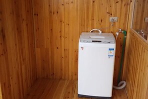 A small, white, compact washer and dryer unit in a wooden room with a wooden floor. - Longji Rice Terraces Weila Homestay (Longsheng)