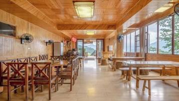 A wooden interior with tables and chairs arranged for dining, large windows offering a view, and a ceiling fan.
