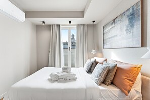 Une chambre d’hôtel avec un lit, une fenêtre avec des rideaux, un tableau au mur et une vue sur la ville.