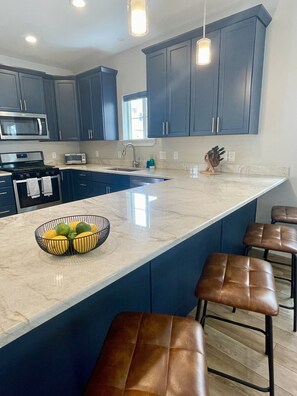 A modern kitchen with dark blue cabinets, a large island with bar stools, a built-in microwave, and a gas stove.